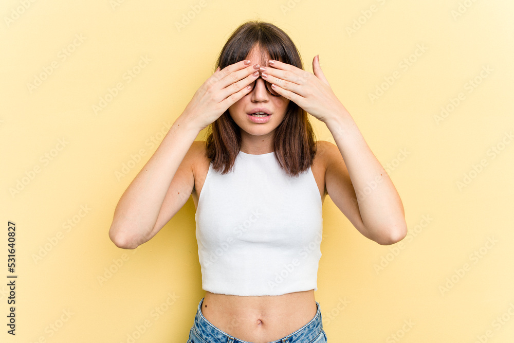 Young caucasian woman isolated on yellow background afraid covering eyes with hands. Young caucasian woman isolated on yellow background afraid covering eyes with hands.
