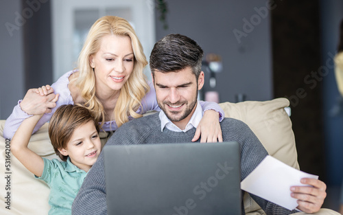 Three member family havign their time in living room Father is working remotely