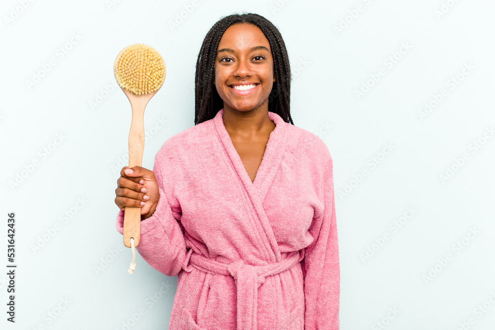 Young African American woman holding a bathtub brush isolated on blue background happy, smiling and cheerful. Young African American woman holding a bathtub brush isolated on blue background happy, smiling and cheerful.