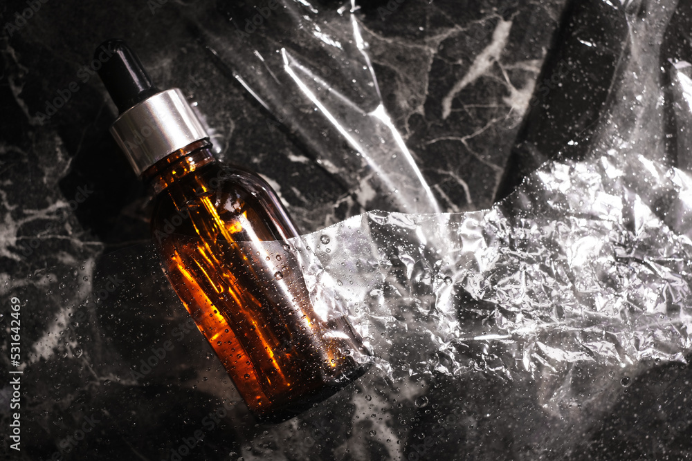 organic cosmetic product in a glass brown bottle with a pipette on a dark marble background