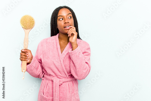 Young African American woman holding a bathtub brush isolated on blue background relaxed thinking about something looking at a copy space.