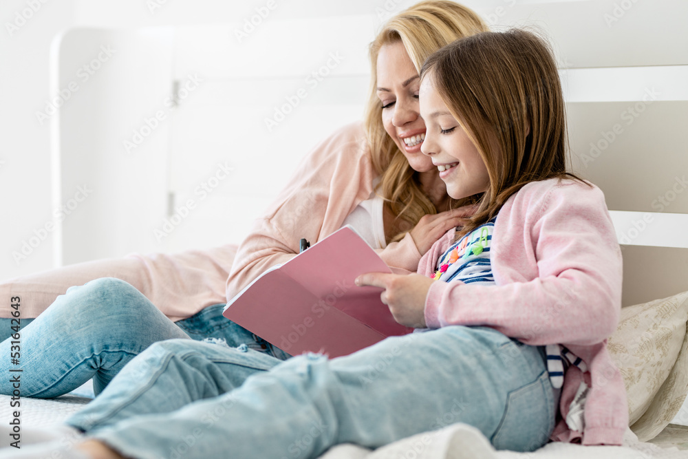 Happy mother with adorable little daughter reeding book on bed Happy mother with adorable little daughter reeding book on bed