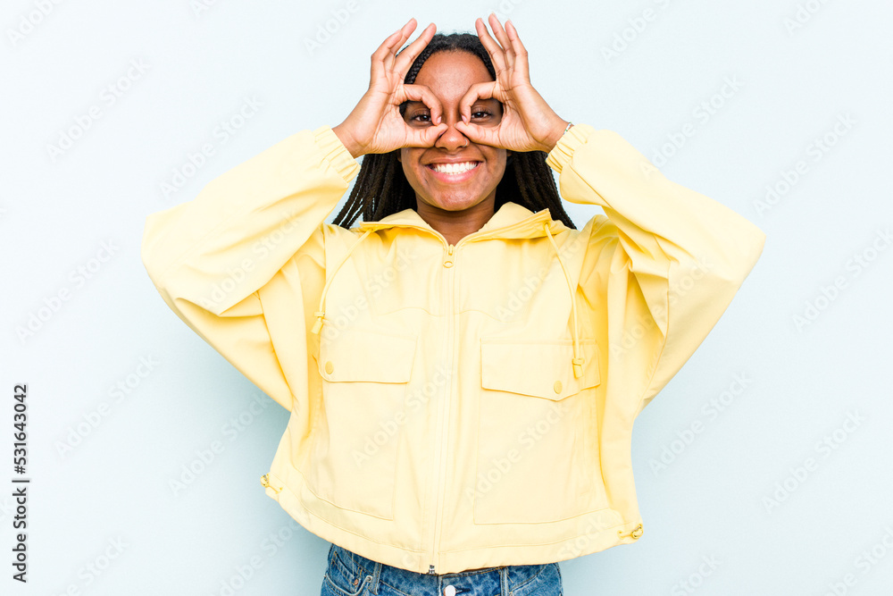 Young African American woman with braids hair isolated on blue background showing okay sign over eyes Young African American woman with braids hair isolated on blue background showing okay sign over eyes