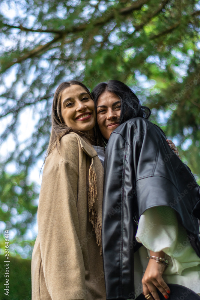 Two friends together happily looking at the camera with tree branches behind them