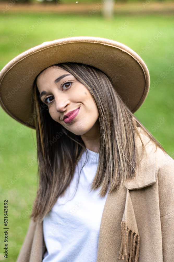 Portrait of cute smiling girl in hat outdoors. Close up of young woman in hat smiling at camera on grass. Face of smiling girl in hat on the grass