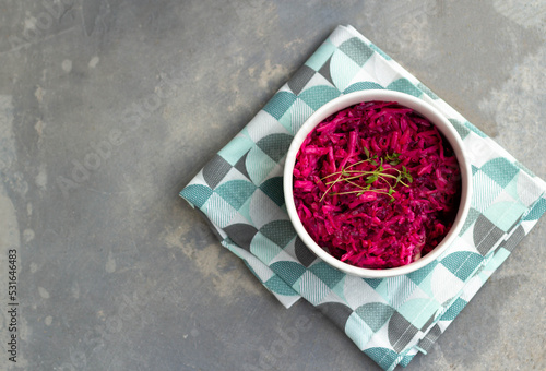 Grated beets with a sprig of thyme in a round bowl on a napkin on a gray background. Top view.