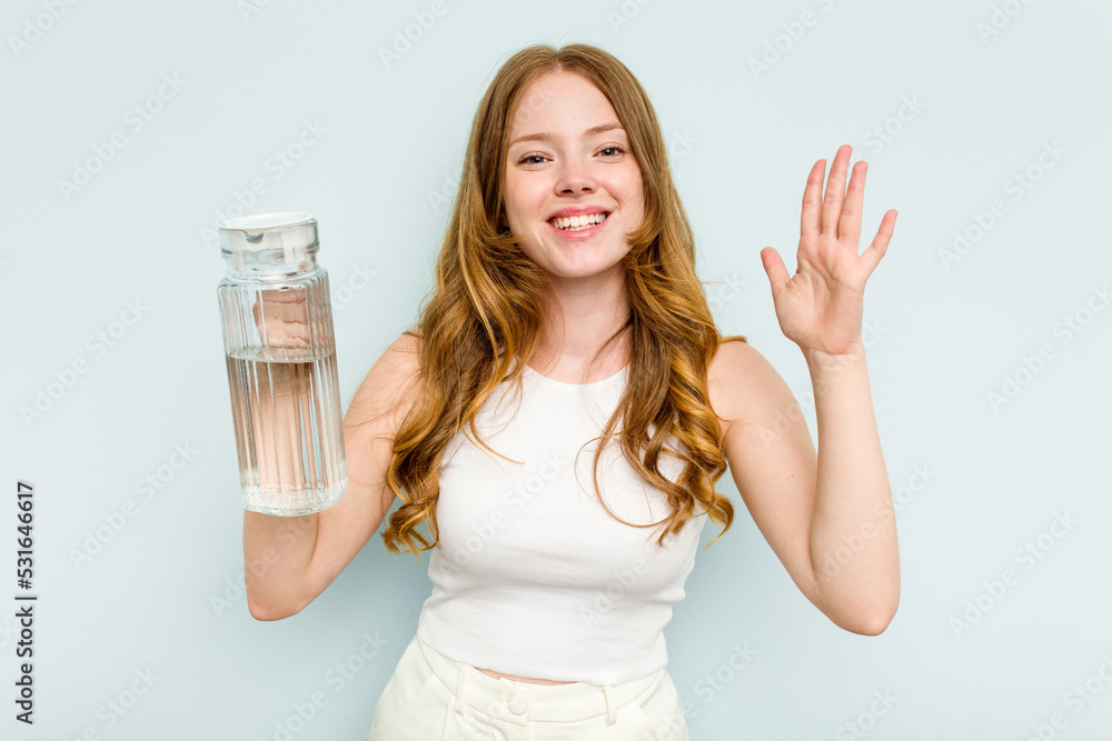 Young caucasian woman holding jar of water isolated on blue background receiving a pleasant surprise, excited and raising hands. Young caucasian woman holding jar of water isolated on blue background receiving a pleasant surprise, excited and raising hands.