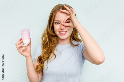 Young caucasian woman holding deodorant isolated on blue background excited keeping ok gesture on eye.