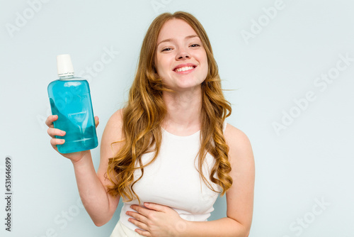 Fotografi Young caucasian woman holding a mouthwash isolated on blue background laughing and having fun