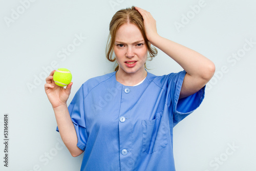 Young caucasian physiotherapist holding a tennis ball isolated on blue background being shocked, she has remembered important meeting. © Asier