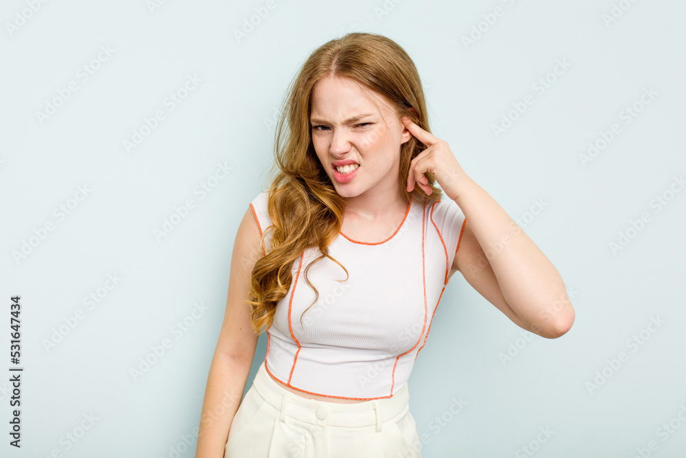 Young caucasian woman isolated on blue background covering ears with fingers, stressed and desperate by a loudly ambient. Young caucasian woman isolated on blue background covering ears with fingers, stressed and desperate by a loudly ambient.