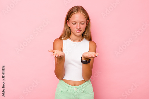 Caucasian teen girl isolated on pink background holding something with palms, offering to camera.