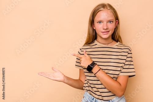 Caucasian teen girl isolated on beige background excited holding a copy space on palm.
