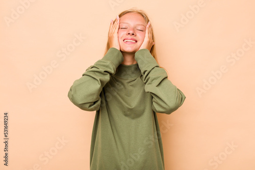 Caucasian teen girl isolated on beige background laughs joyfully keeping hands on head. Happiness concept. © Asier