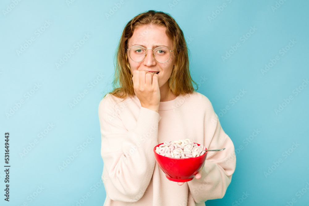 Young caucasian woman holding a bowl of cereals isolated on blue background biting fingernails, nervous and very anxious. Young caucasian woman holding a bowl of cereals isolated on blue background biting fingernails, nervous and very anxious.
