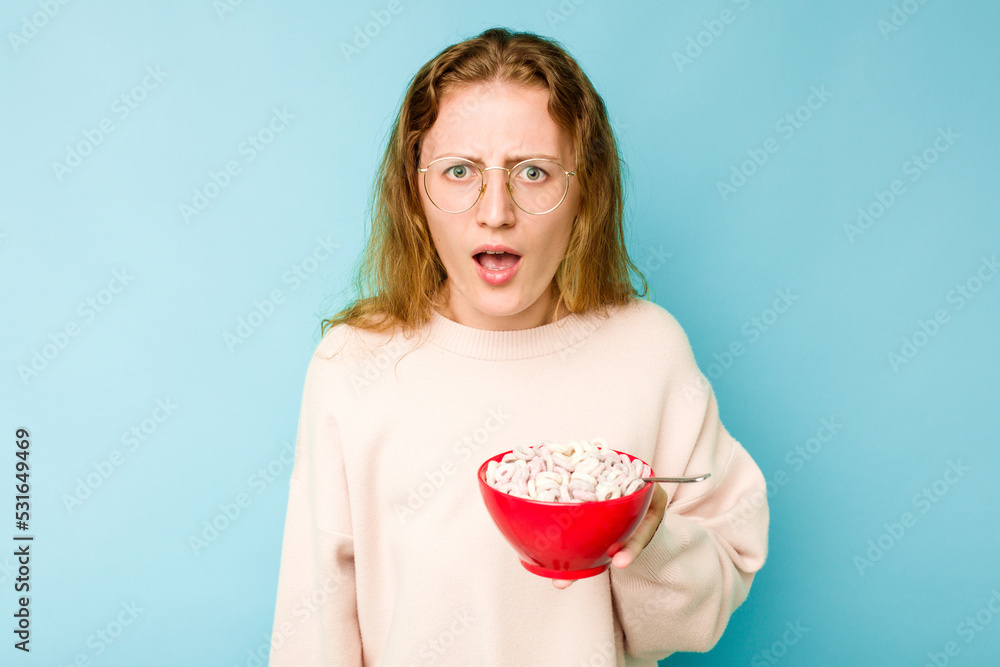 Young caucasian woman holding a bowl of cereals isolated on blue background screaming very angry and aggressive. Young caucasian woman holding a bowl of cereals isolated on blue background screaming very angry and aggressive.