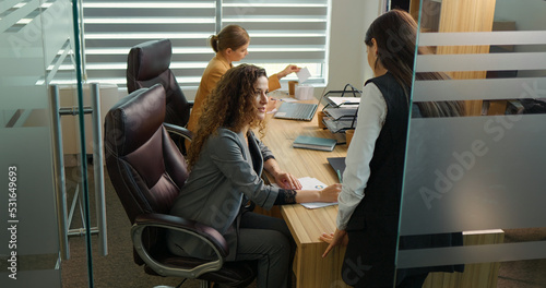 Two business ladies sharing news about best sold product in their firms. Strict female boss giving orders and work tasks to new team member at workplace. photo