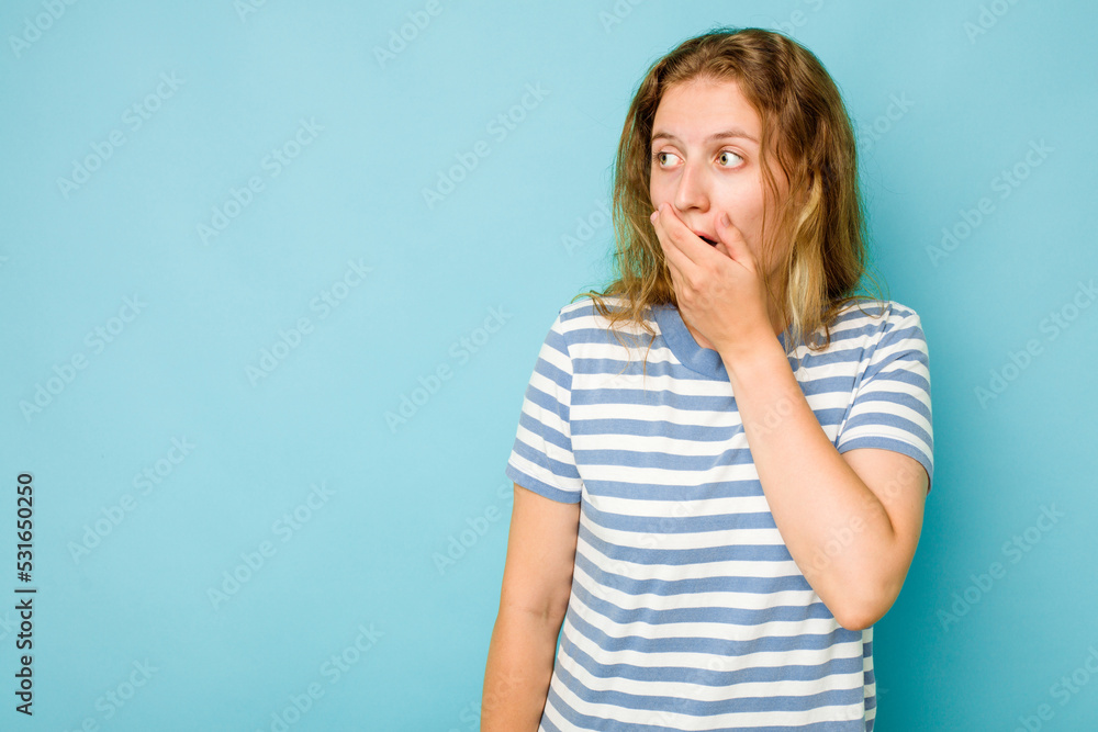 Young caucasian woman isolated on blue background thoughtful looking to a copy space covering mouth with hand. Young caucasian woman isolated on blue background thoughtful looking to a copy space covering mouth with hand.