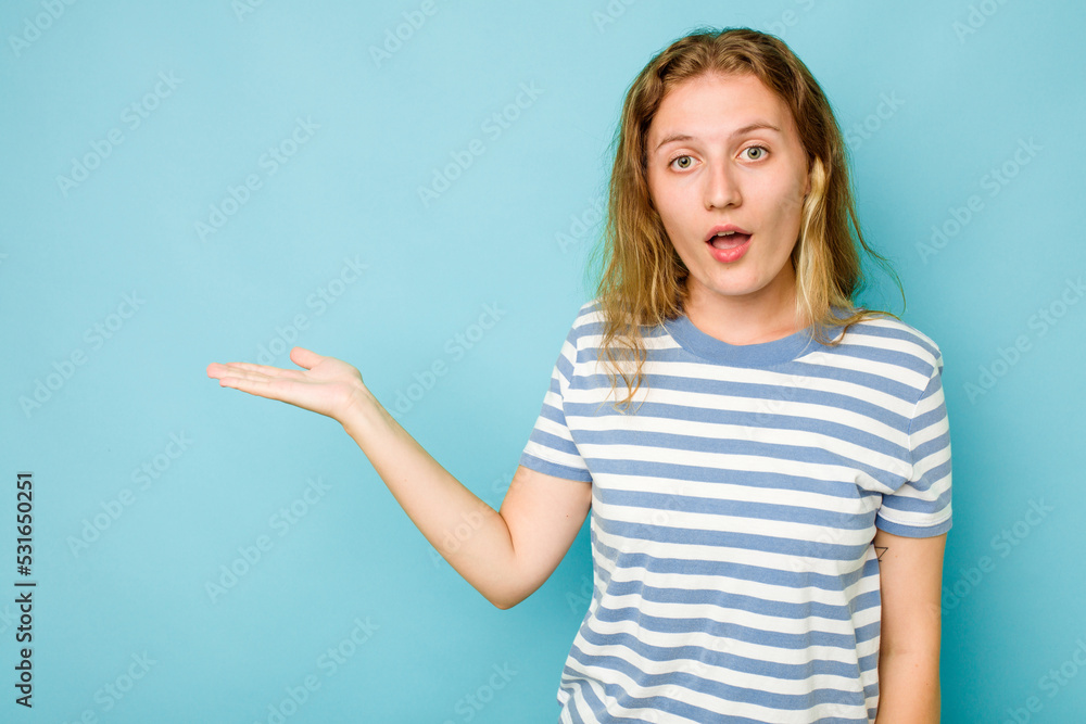 Fototapeta premium Young caucasian woman isolated on blue background impressed holding copy space on palm.