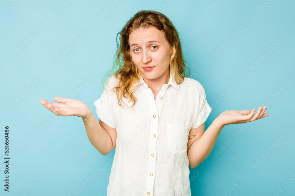 Young caucasian woman isolated on blue background doubting and shrugging shoulders in questioning gesture. Young caucasian woman isolated on blue background doubting and shrugging shoulders in questioning gesture.