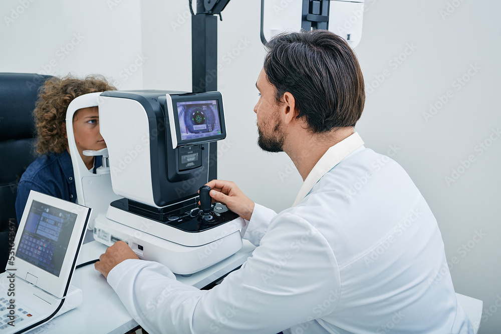 Obraz premium Optometrist using autorefractor determining required level of vision correction and determining individual's prescription for glasses for male child