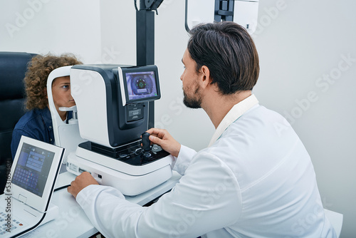 Optometrist using autorefractor determining required level of vision correction and determining individual's prescription for glasses for male child photo