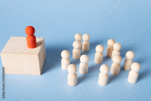 A red figure stands on a pedestal addressing a group of identical figures. The concept of leadership, recitation, meetings