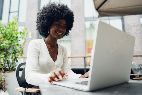 Smiling young african woman sitting with laptop in coffee shop