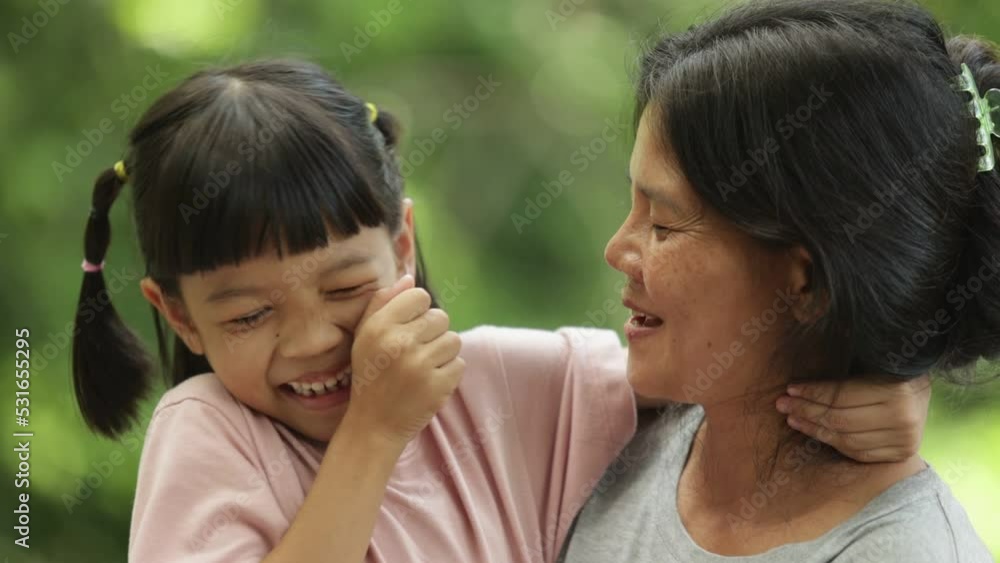 Portrait of a Thai mother and daughter of Asian descent are sitting in the outdoor park happily and cheerfully smiling face Be a loving mother a warm family The background is green trees. Portrait of a Thai mother and daughter of Asian descent are sitting in the outdoor park happily and cheerfully smiling face Be a loving mother a warm family The background is green trees.