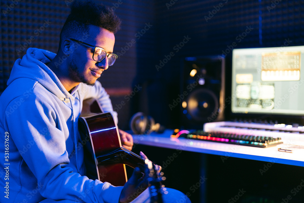 Male vocal artist, singer, with curly hair playing on guitar in sound studio recording new melody or album. Male vocal artist, singer, with curly hair playing on guitar in sound studio recording new melody or album.