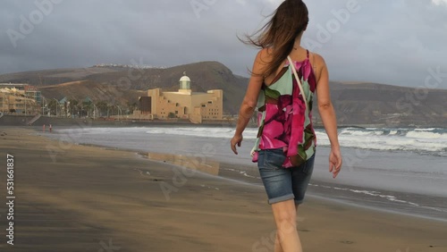 Cinematic shot at dawn of a woman walking on the beach of Las Canteras and in the background you can see the Alfredo Kraus Auditorium. Located in the city of Las Palmas on the island of Gran Canaria. photo