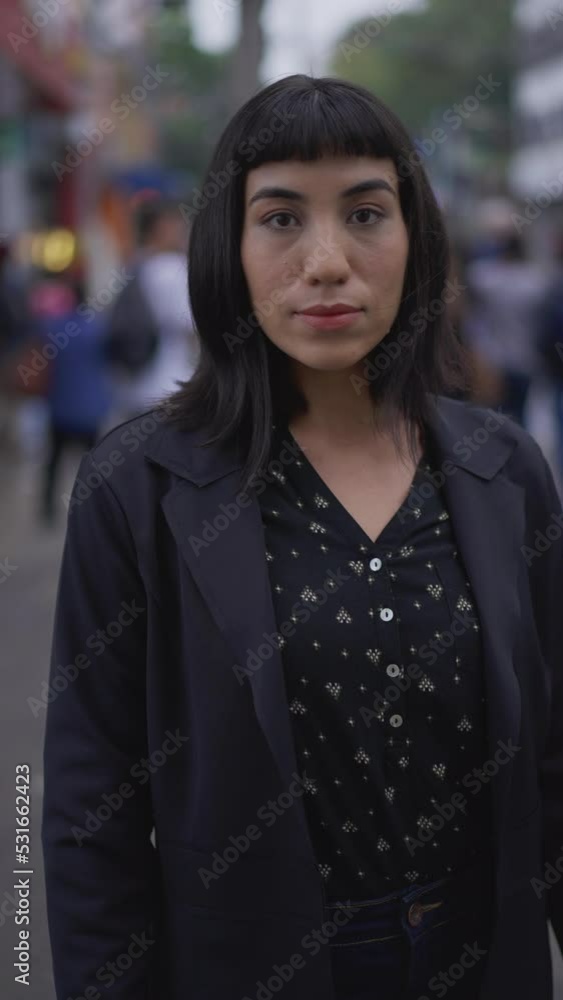 One hispanic young woman standing in street. South American latina Brazilian female person closeup face with serious expression looking at camera in Vertical Video One hispanic young woman standing in street. South American latina Brazilian female person closeup face with serious expression looking at camera in Vertical Video
