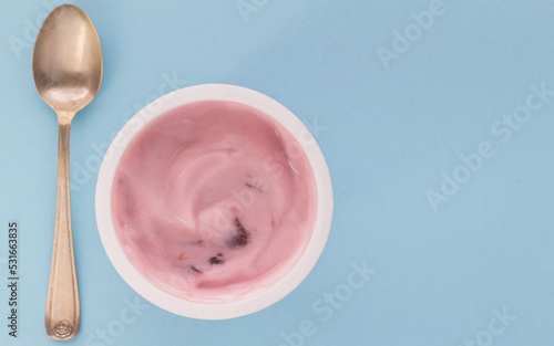 Yogurt cup with pink strawberry yoghurt isolated on baby blue background with copy space - selective focus image