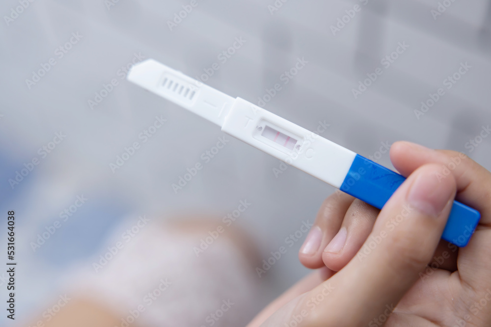 Fototapeta premium Female Hand Holding Positive Pregnancy Test on the Toilet