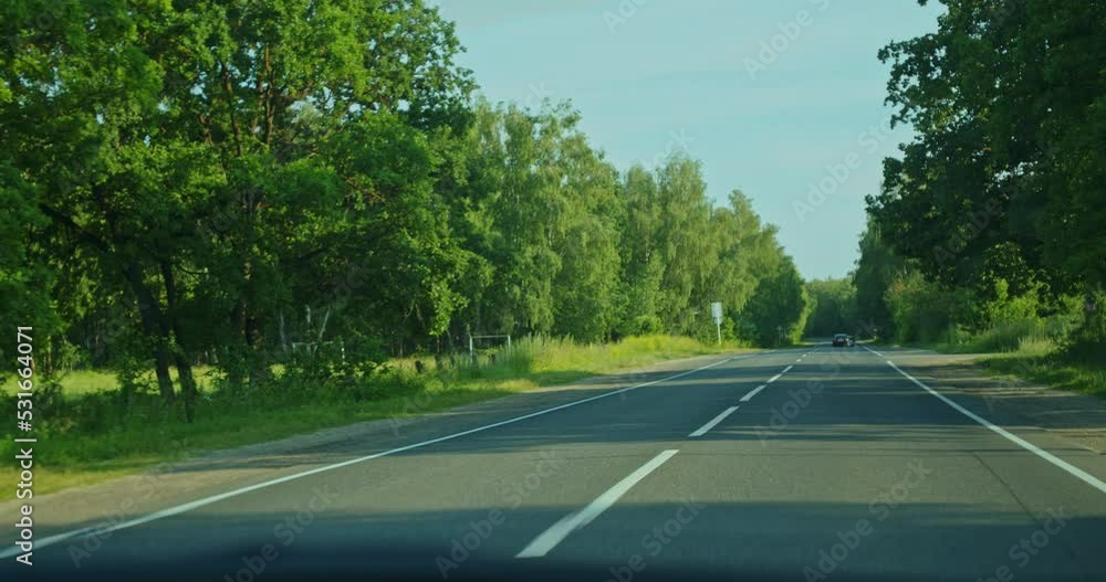 Driving in the first person, the driver is driving along a summer highway, on a beautiful sunny day, among a dense forest. View from the salon.