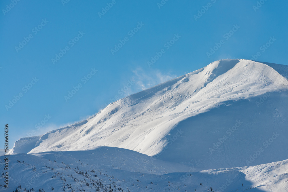 Snow-covered mountain top. The wind rises the snow on the mountain range.