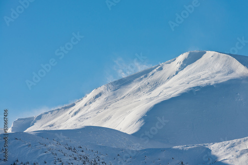 Snow-covered mountain top. The wind rises the snow on the mountain range.