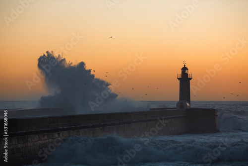 Lighthouse, washed in the sunset by a wave. Porto, Portugal.