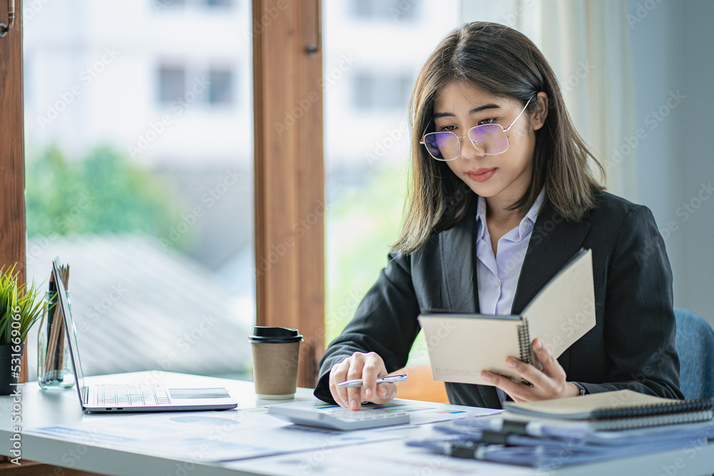 Asian business woman Use a laptop computer and work at the office with the calculator documents on the desk. plan to analyze financial reports Asian business woman Use a laptop computer and work at the office with the calculator documents on the desk. plan to analyze financial reports