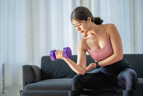 Asian woman in sportswear sitting relaxing and practicing yoga and exercising with dumbbells and laptop computer in bedroom at home fitness concept