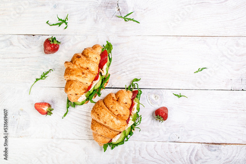 croissant sandwich with strawberries, arugula, avocado and brie, camembert cheese. banner menu recipe place for text, top view.