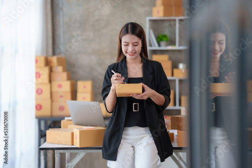 Asian online business owner Prepare parcel boxes for customers. Check the balance and correct shipping address and phone number and save the data using a laptop computer.
