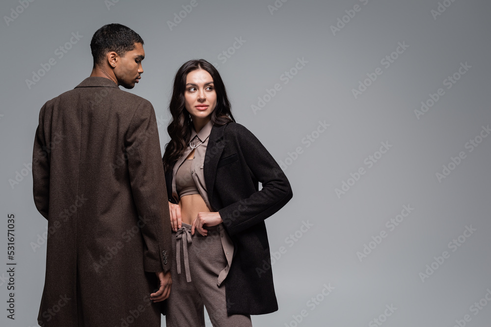 young african american man in woolen coat near stylish woman in black blazer isolated on grey.
