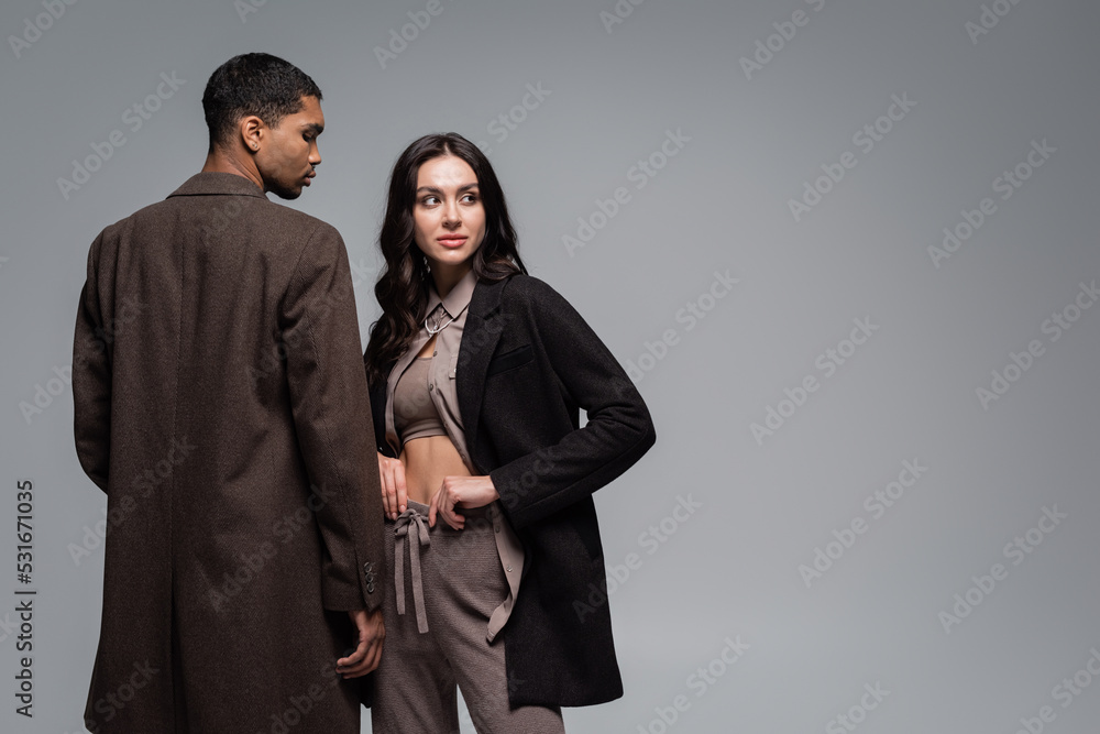 young african american man in woolen coat near stylish woman in black blazer isolated on grey. young african american man in woolen coat near stylish woman in black blazer isolated on grey.