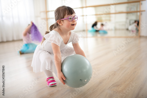 Foto Little girl with down syndrome playing with ball at ballet class in dance studio