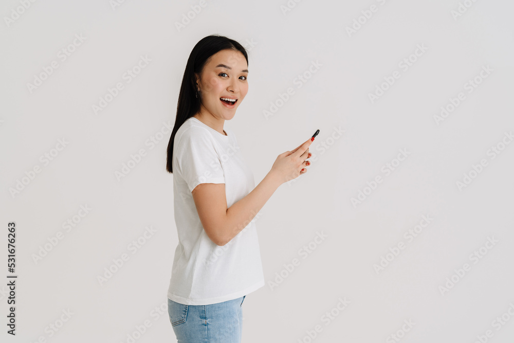 Asian excited woman wearing t-shirt smiling and using cellphone Asian excited woman wearing t-shirt smiling and using cellphone
