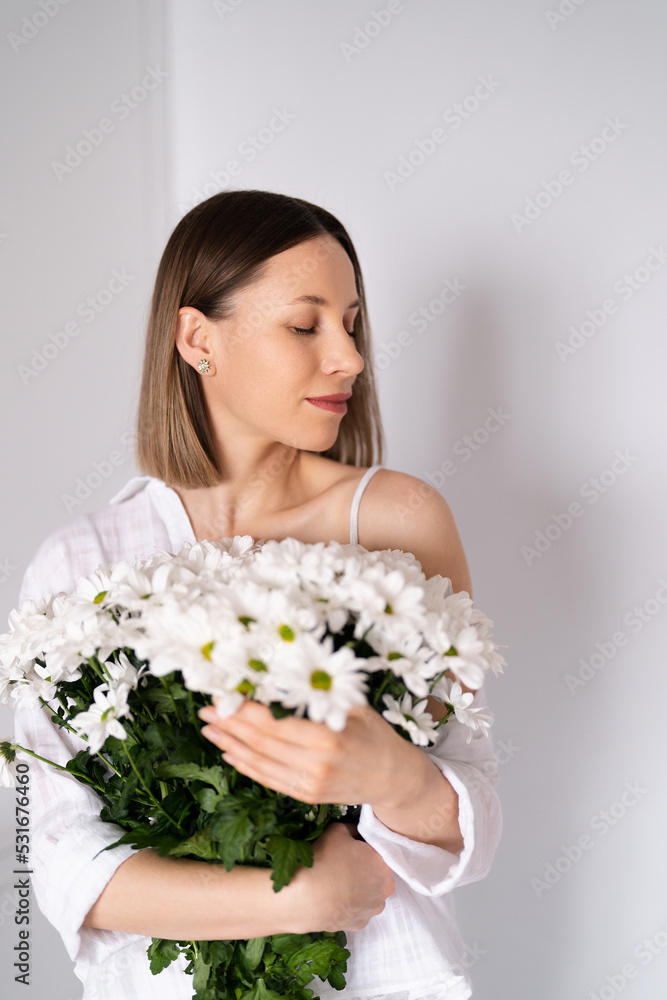 Young beautiful cute sweet lovely smiling woman with hold a bouquet of white fresh flowers on white wall background Young beautiful cute sweet lovely smiling woman with hold a bouquet of white fresh flowers on white wall background