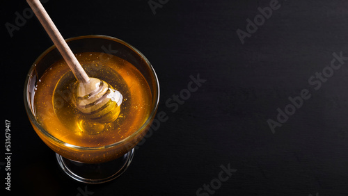 Honey in a glass bowl with honey dipper on a dark background. Space for text. Copy space