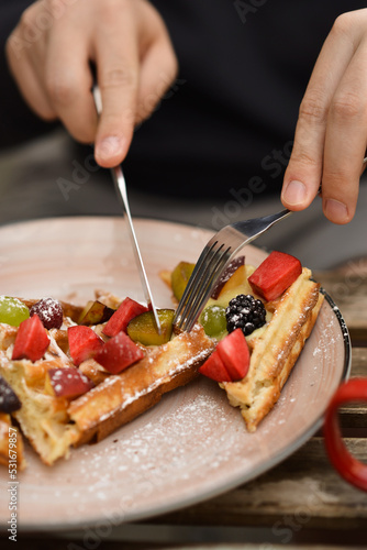 A man cuts a sweet wafer with fruits in a cafe