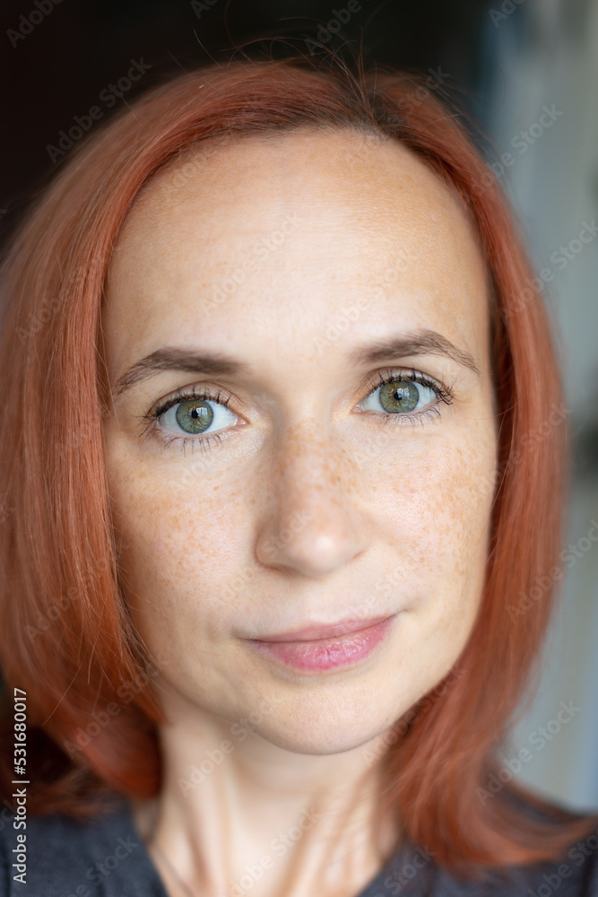 Young pretty woman with red hair, green eyes and freckles looks at the camera and smiles. Close-up, selective focus. Young pretty woman with red hair, green eyes and freckles looks at the camera and smiles. Close-up, selective focus.